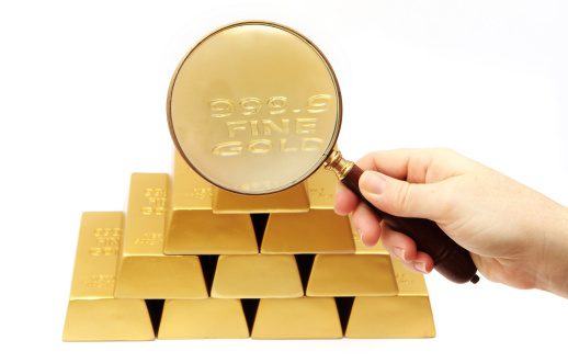 Gold ingots on a white background with magnifying glass