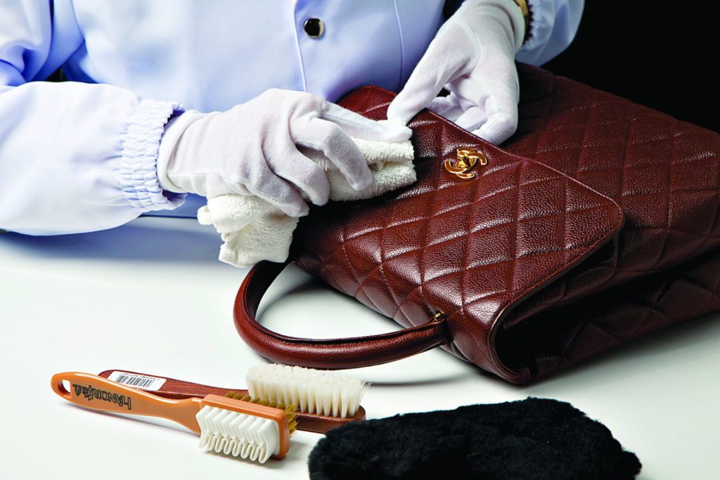 Person Cleaning Designer Handbag With Clothe